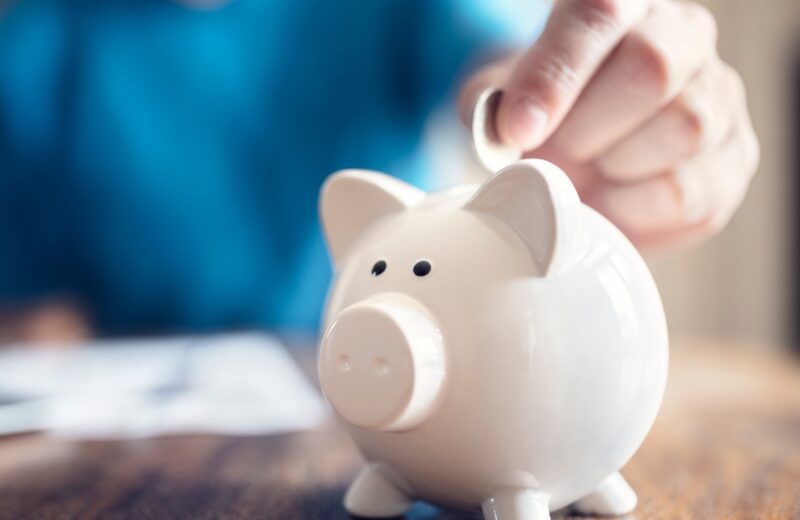 A person sitting at a table putting a coin in a piggy bank