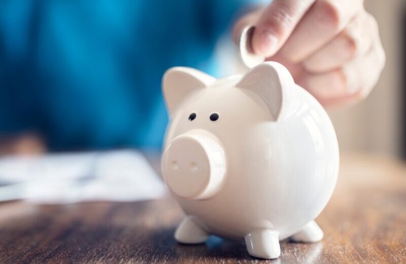 A person sitting at a table putting a coin in a piggy bank