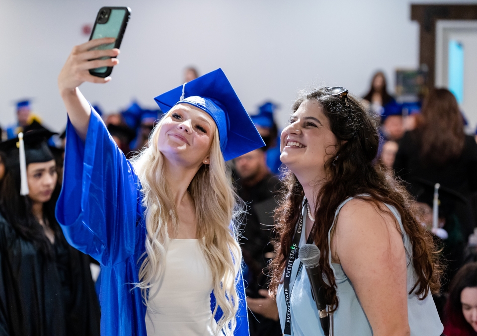 Employee and a student posing for a selfie at graduation