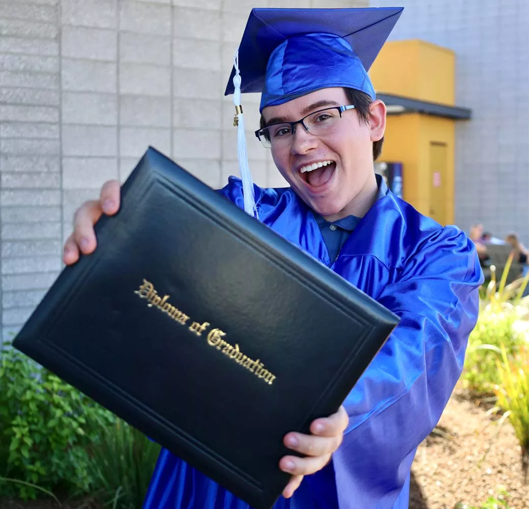Student smiling while holding their high school diploma