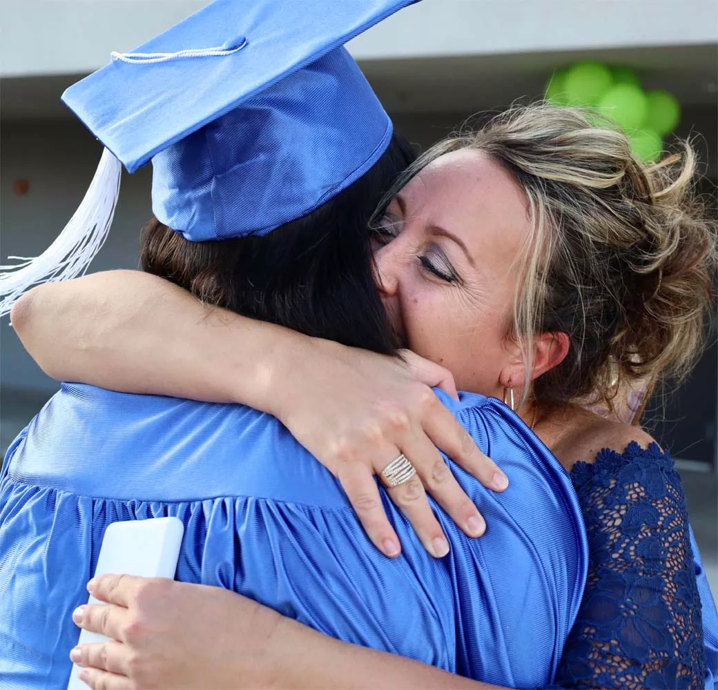 A mentor is hugging one of their students on their graduation day