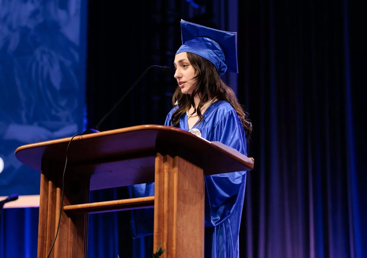 Graduate speaking at a podium, on stage at their graduation