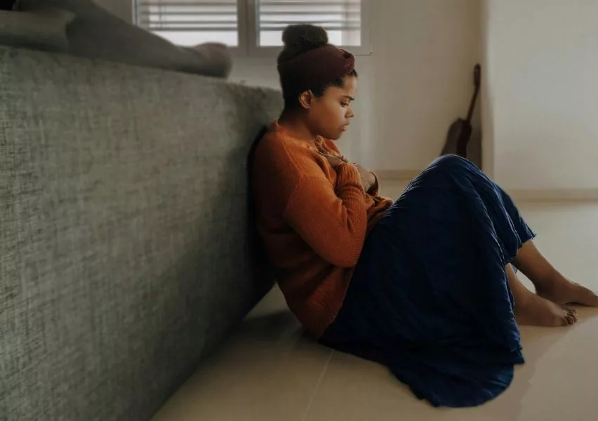 Student feeling anxiety as she sits on the floor leaning against a couch