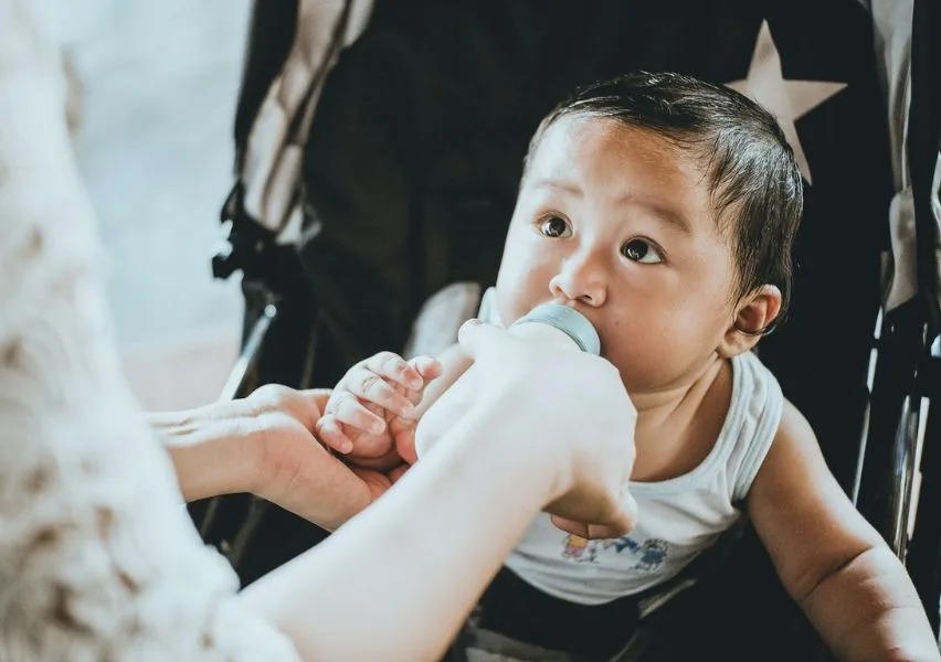 Caregiver giving a pacifier to an infant while another holds him