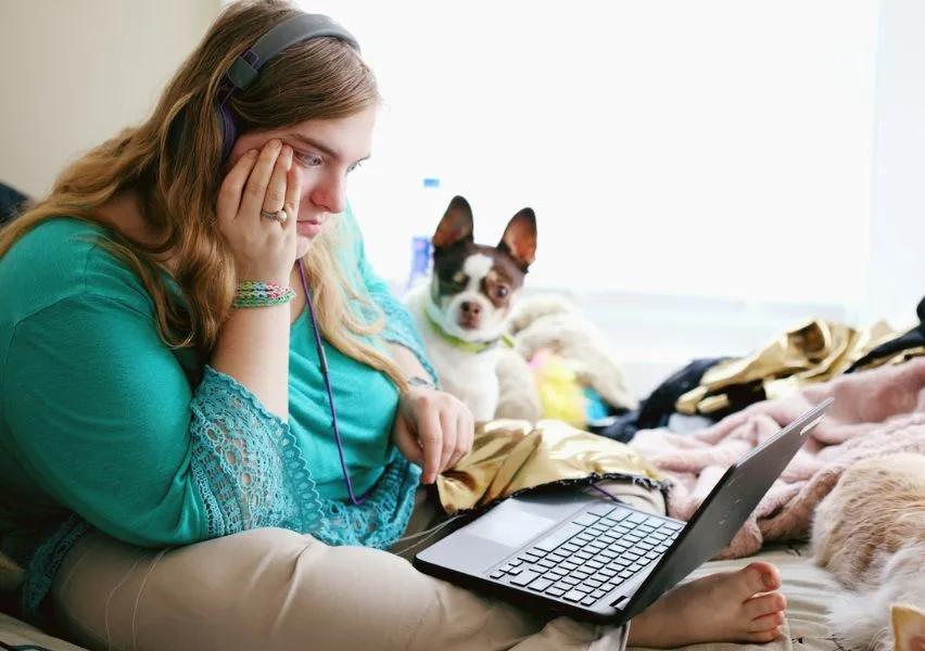 Student attending online school at home in bed with their dog