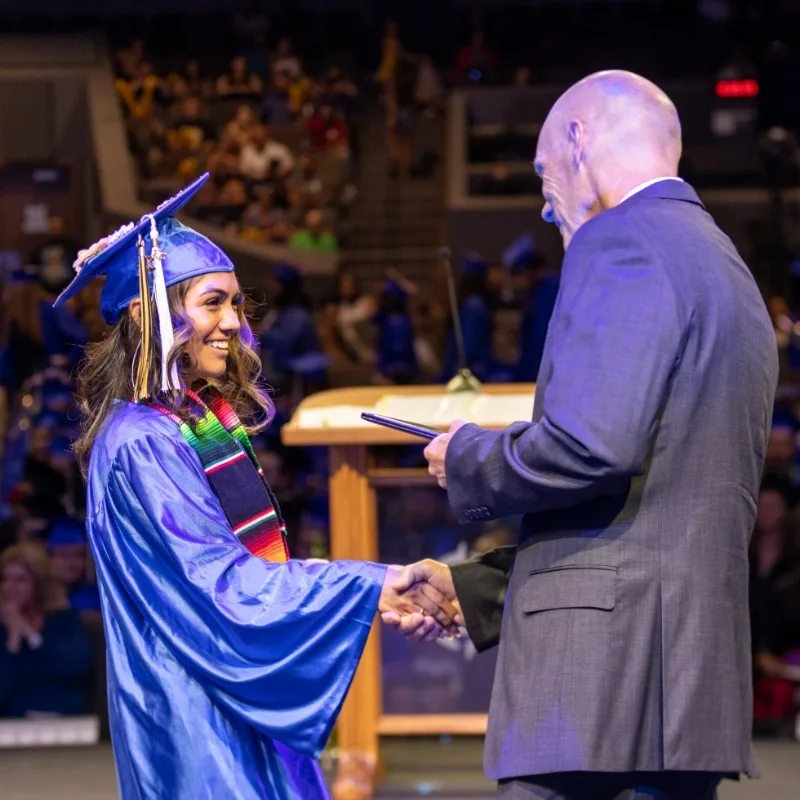 High school Graduation ceremony showing a young woman shaking a man's hand on stage
