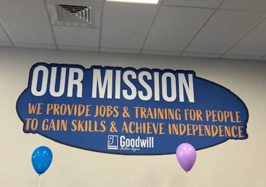 Sign on an interior wall listing Goodwill's mission: "We provide jobs & training for people to gain skills & achieve independence"