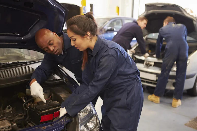 Teacher Helping Female Student Training To Be Car Mechanics