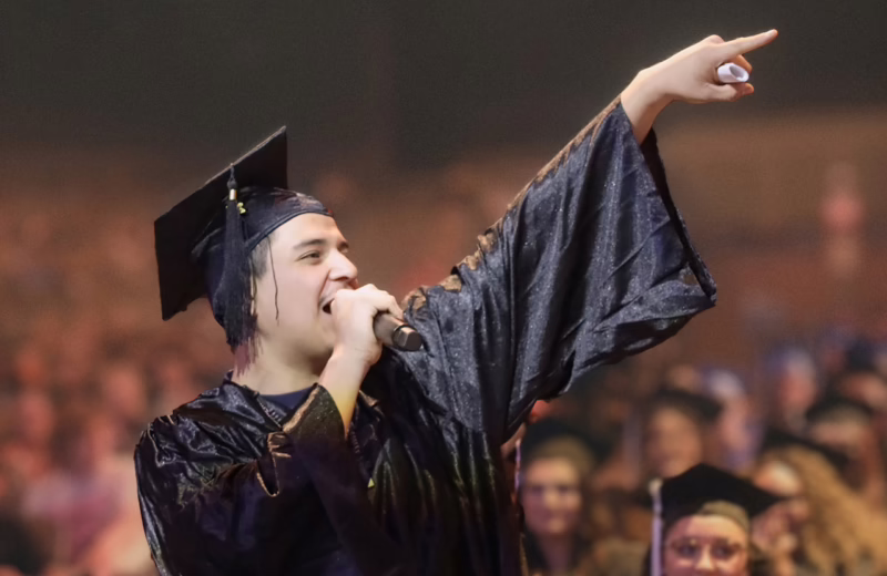 Smart Schools student speaking into a mic and pointing at their family at a graduation ceremony